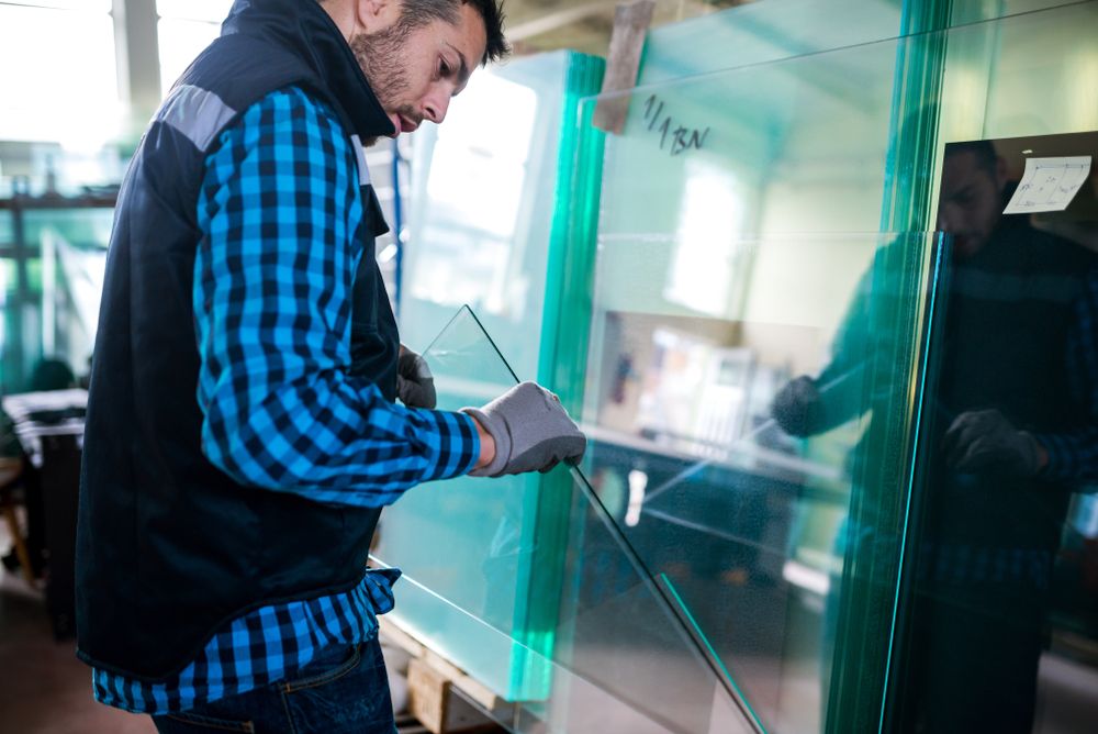 A Man Is Working On A Piece Of Glass In A Factory — New England Glass & Aluminium In Walcha, NSW