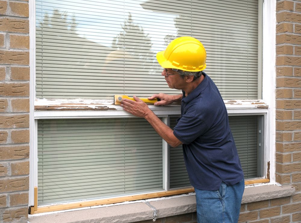 A Man Wearing A Hard Hat Is Measuring A Window With A Tape Measure — New England Glass & Aluminium In Gunnedah, NSW