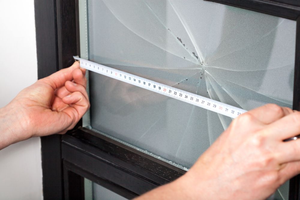 A Person Is Measuring A Broken Window With A Tape Measure — New England Glass & Aluminium In Armidale, NSW