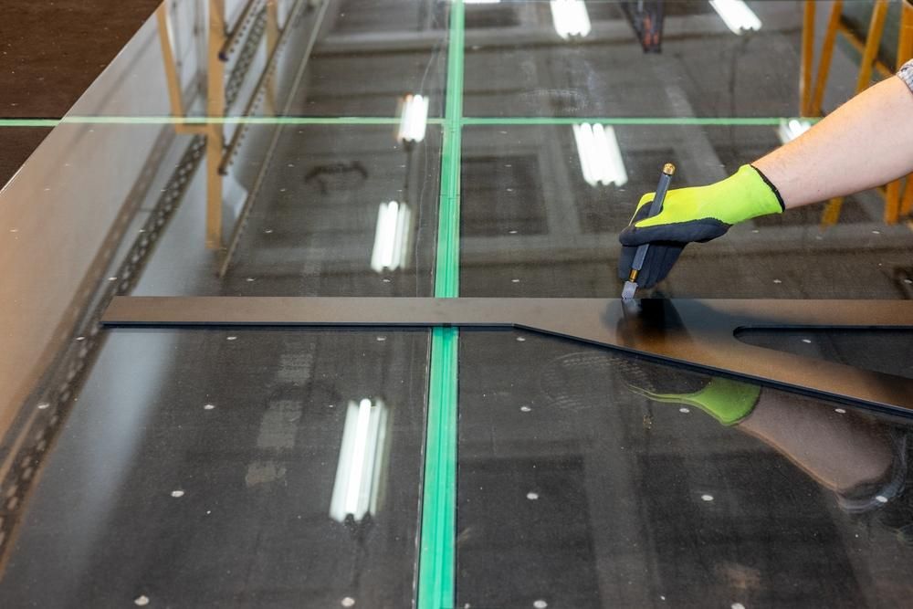 A Person Wearing Yellow Gloves Is Cutting a Piece of Glass — New England Glass & Aluminium In Armidale, NSW