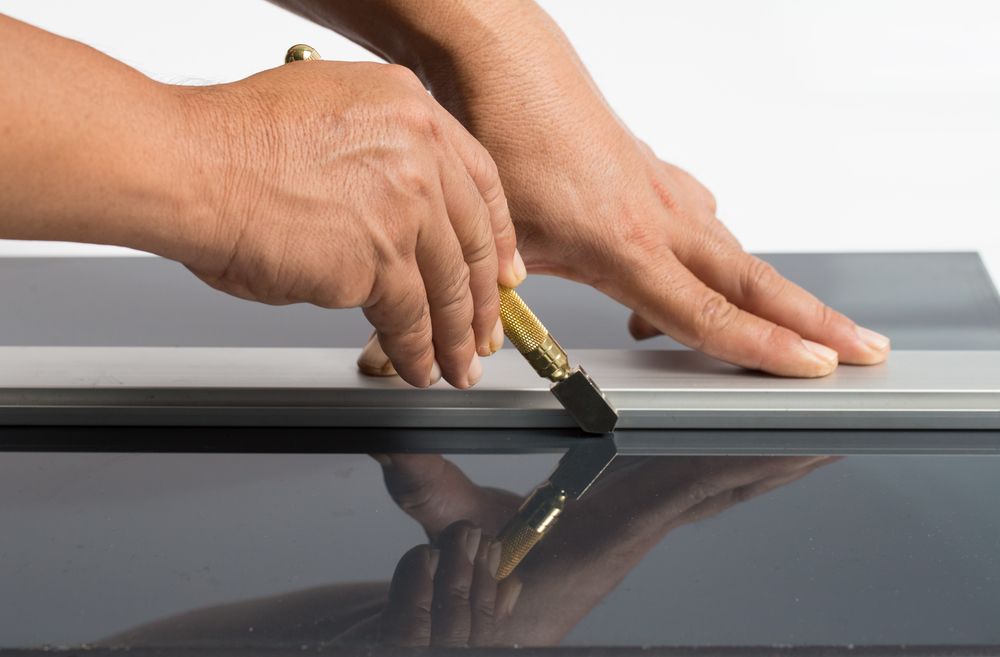 A Person Is Cutting A Piece Of Glass With A Glass Cutter — New England Glass & Aluminium In Armidale, NSW