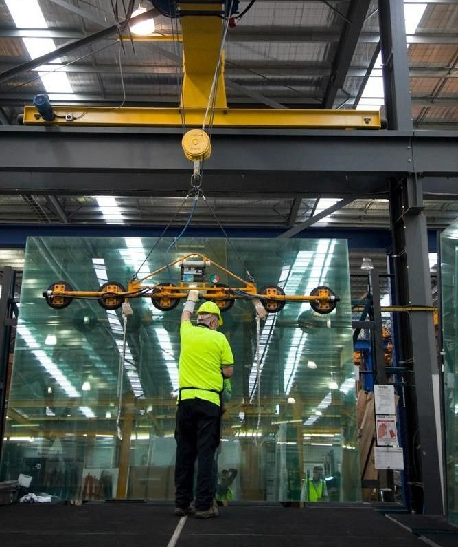 A Man Is Standing Under A Crane In A Factory Holding A Piece Of Glass — New England Glass & Aluminium In Armidale, NSW