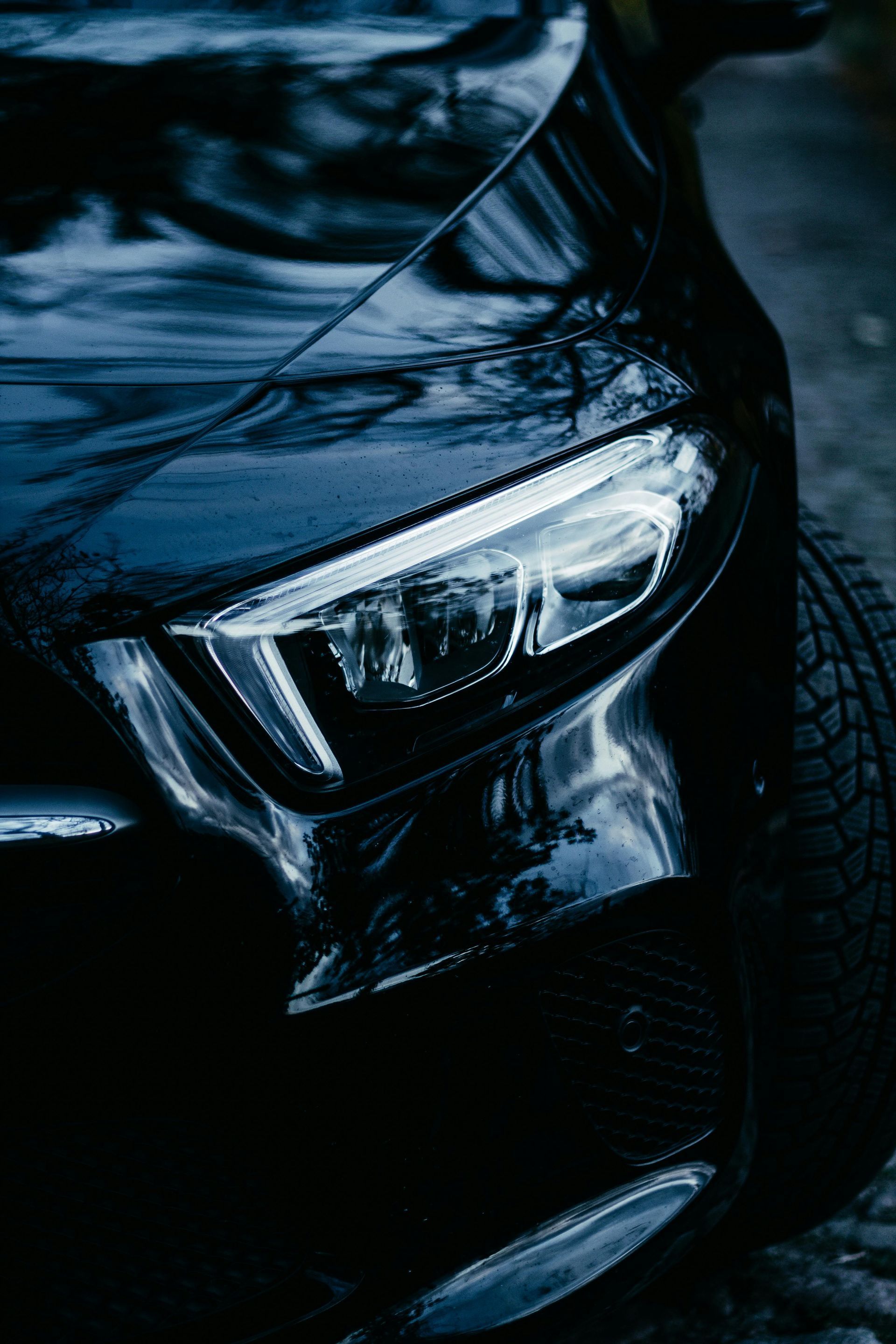 Black car headlight and front panel, close-up shot, reflecting ambient light.