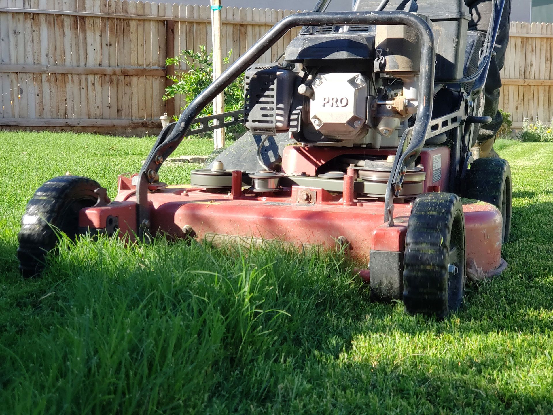 A red commercial lawn mower sits on a green lawn in front of a wooden fence.