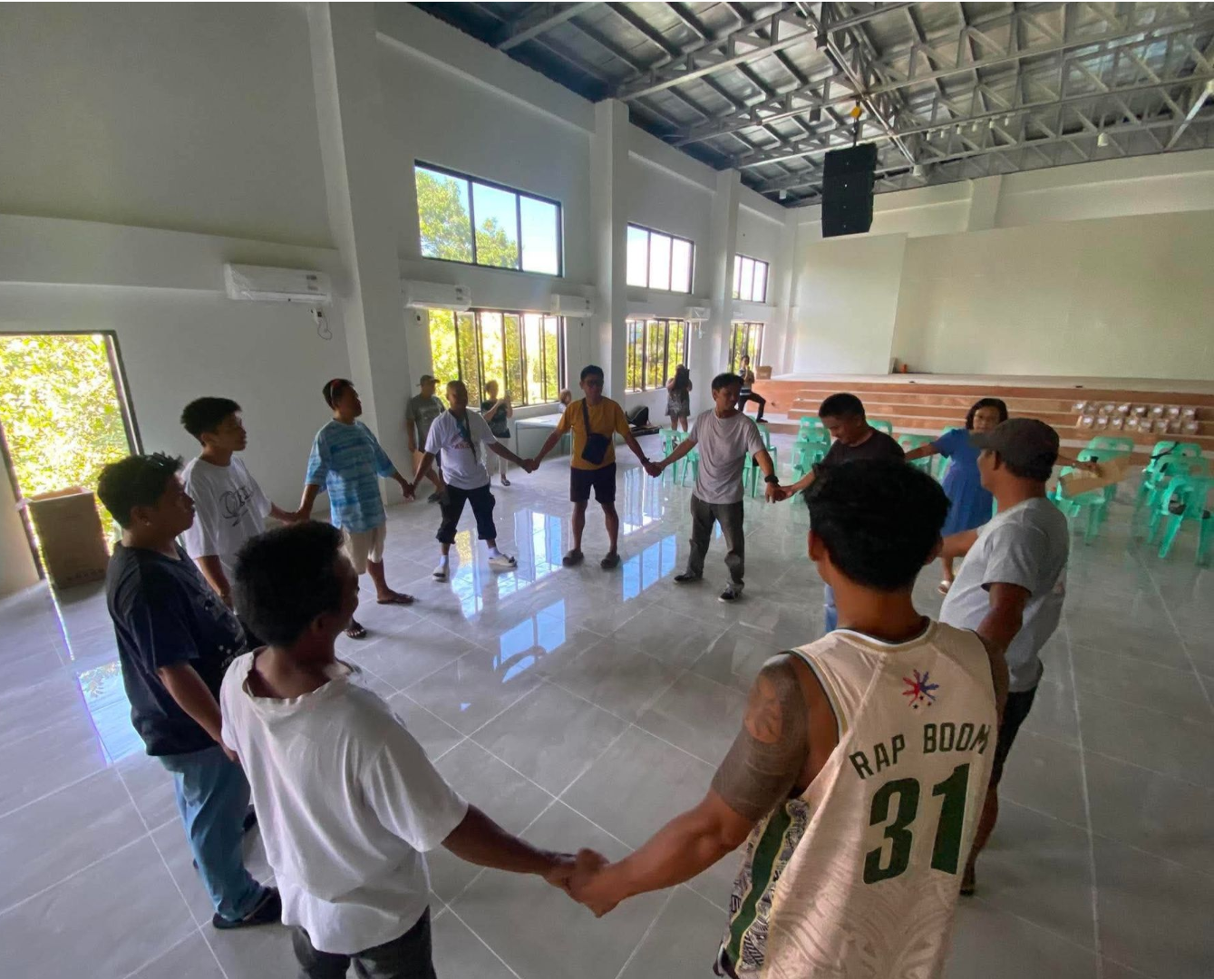 Students holding hands in a bright gym, standing in a circle during an activity
