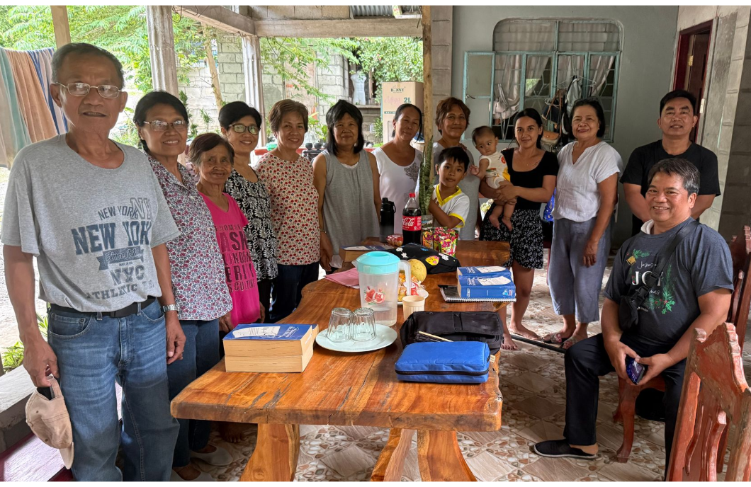 Group of people gathered around a table with food and a cake in a covered outdoor area