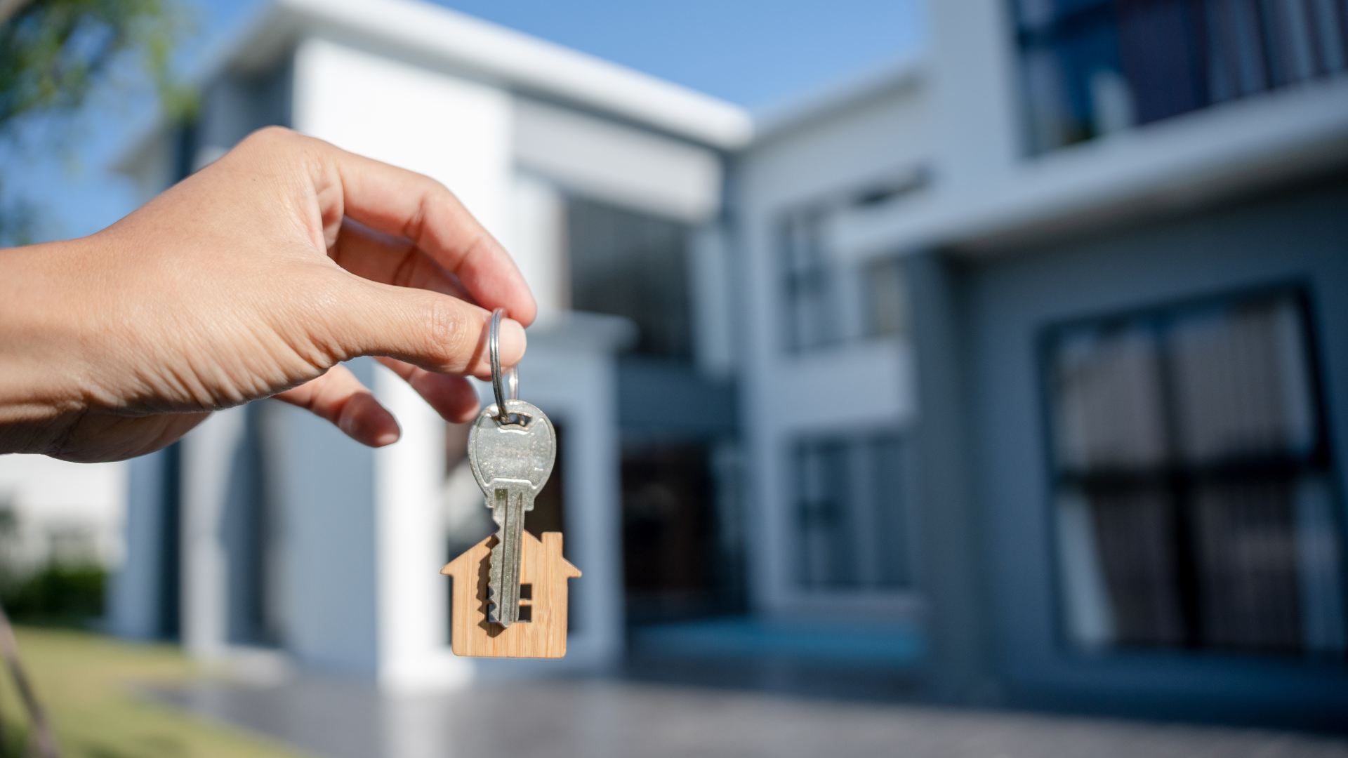 Hand holding house keys with house in the background.