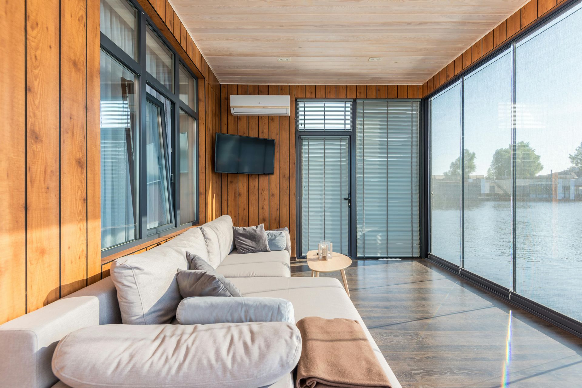 Cozy sunroom with a sectional sofa, TV, and large windows. Wooden walls, neutral colors overlooking Hayden Lake