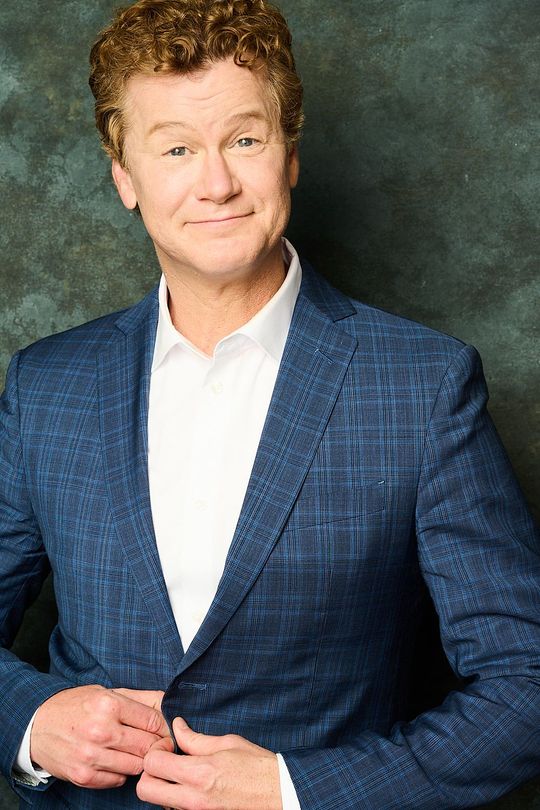 Jonathan Mangum in a blue suit and white shirt is smiling.