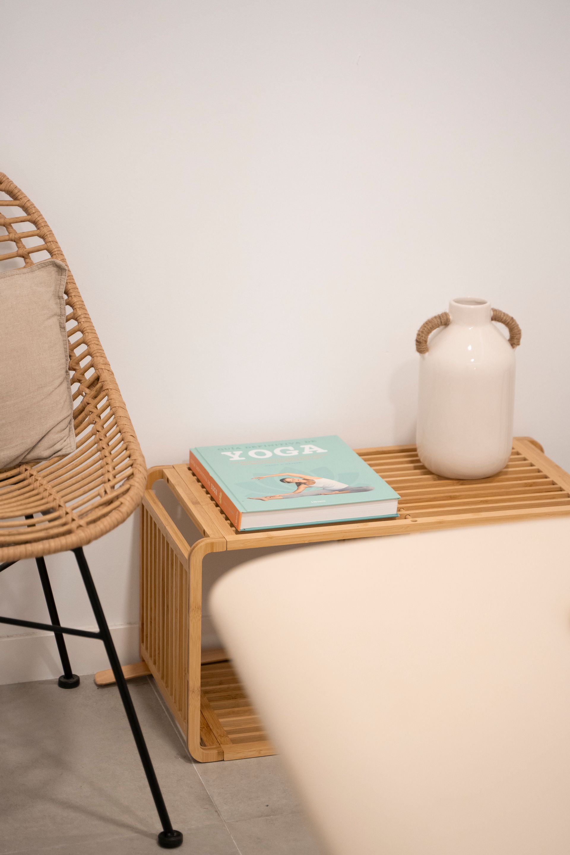 Una silla de mimbre está al lado de una mesa de madera con un libro encima.