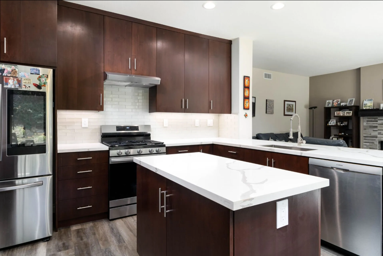 Modern kitchen with dark wood cabinets, stainless steel appliances, and a large white island countertop