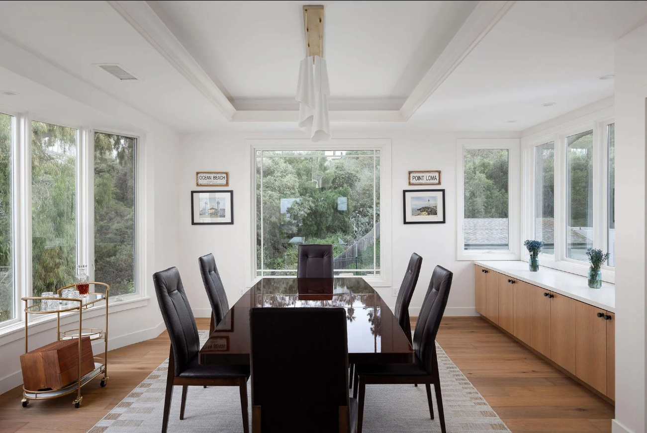 Bright dining room with long table, dark chairs, large windows, and wood sideboard across the back wall