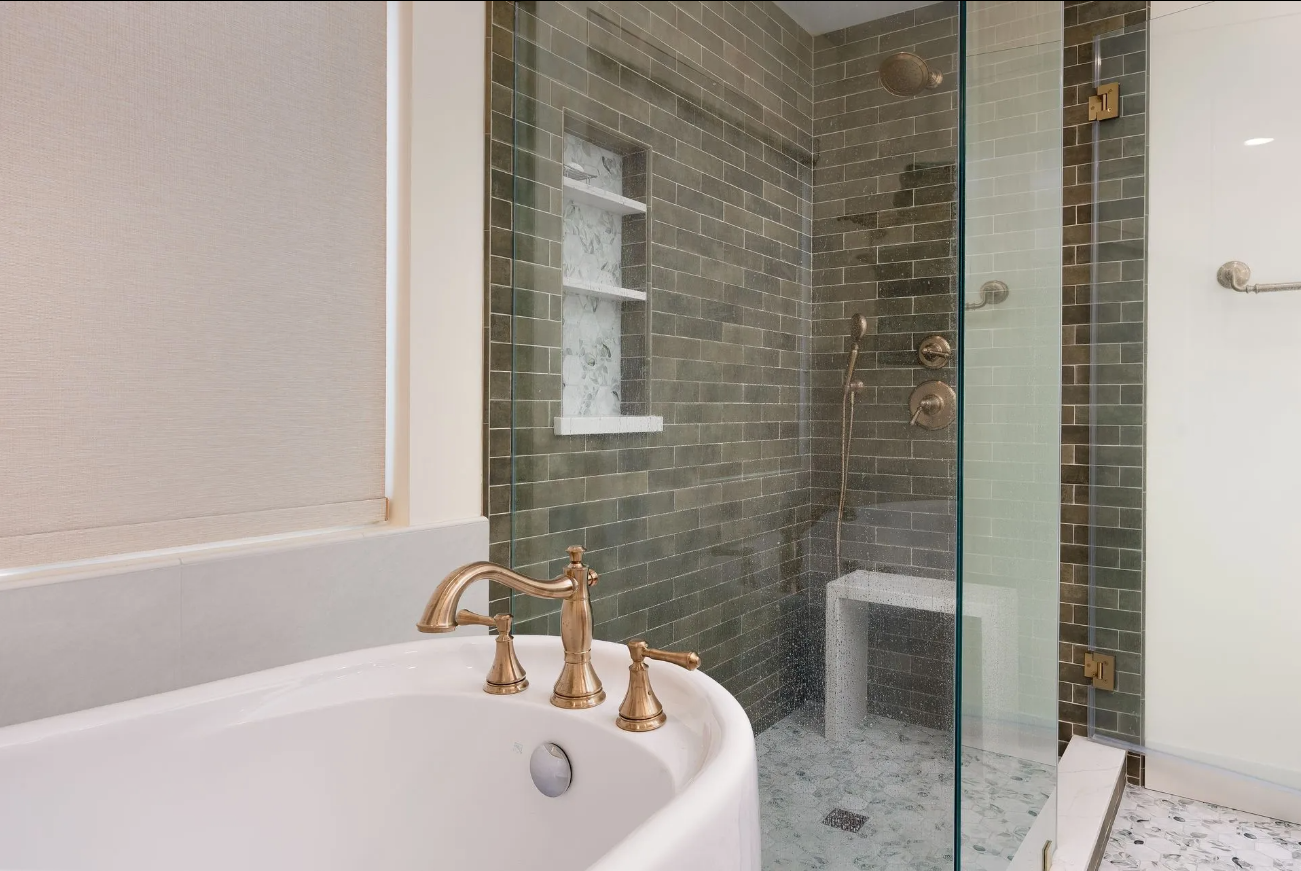 Bathroom vanity beside a glass-enclosed shower with gray tile and gold fixtures
