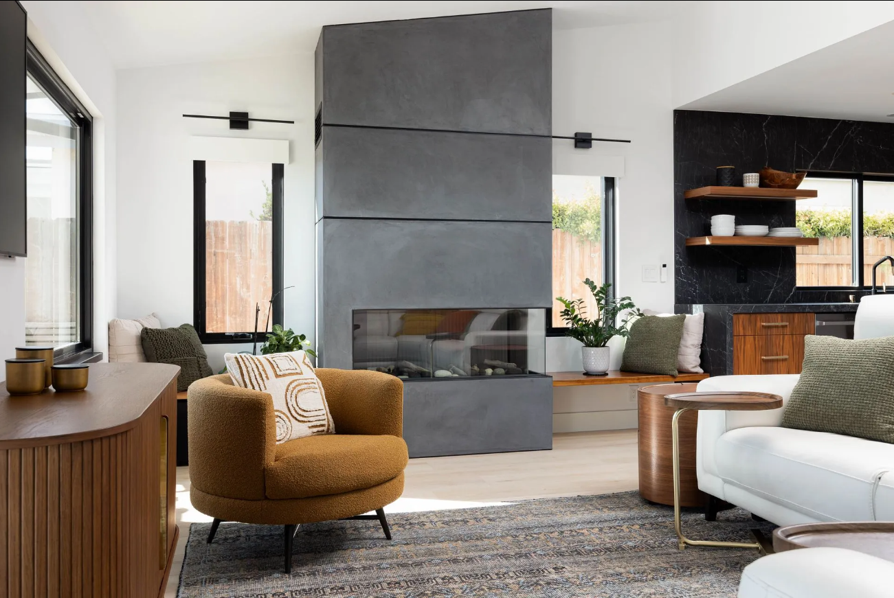Modern living room with a large gray fireplace, mustard chair, white sofa, and wood shelving