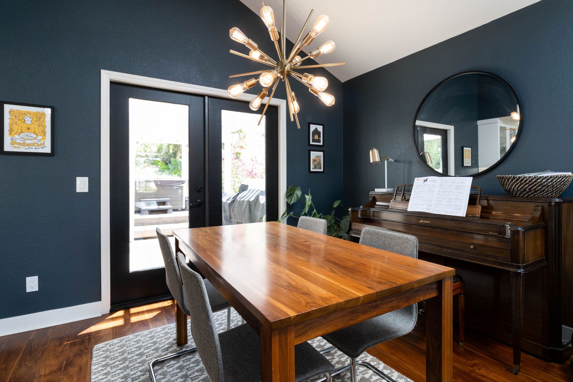Dining room with a wooden table, chandelier, piano, and dark blue walls near glass doors.