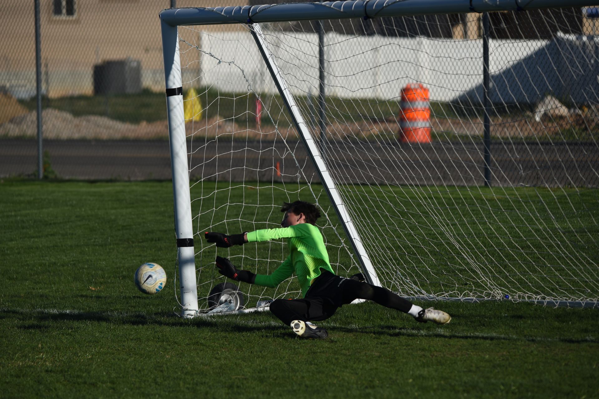 Rampage Soccer goalie in green dives to block a ball near the goal on a green field.