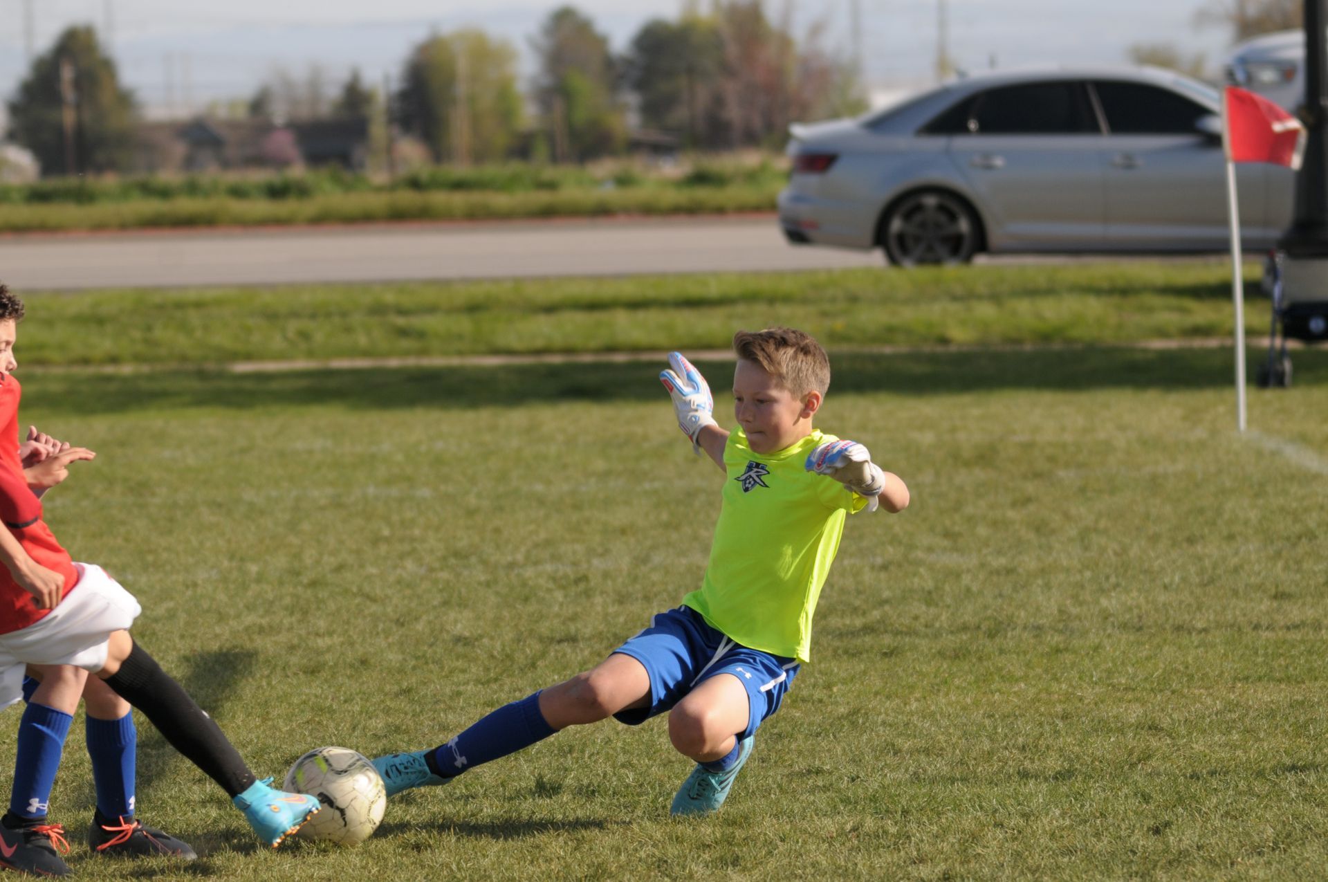 Rampage keepr in yellow soccer uniform sliding on grass field, attempting to kick ball.