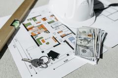 Floor plan with house keys, dollar bills, and a white model home on a desk
