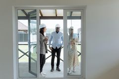 Three people in hard hats stand in a bright room near a sliding glass door, discussing the site.