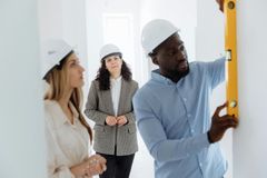 Three workers in hard hats inspecting a wall with a measuring level