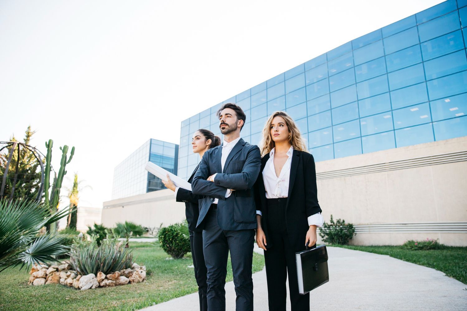 Three business professionals walking outside a modern glass office building, one holding a folder
