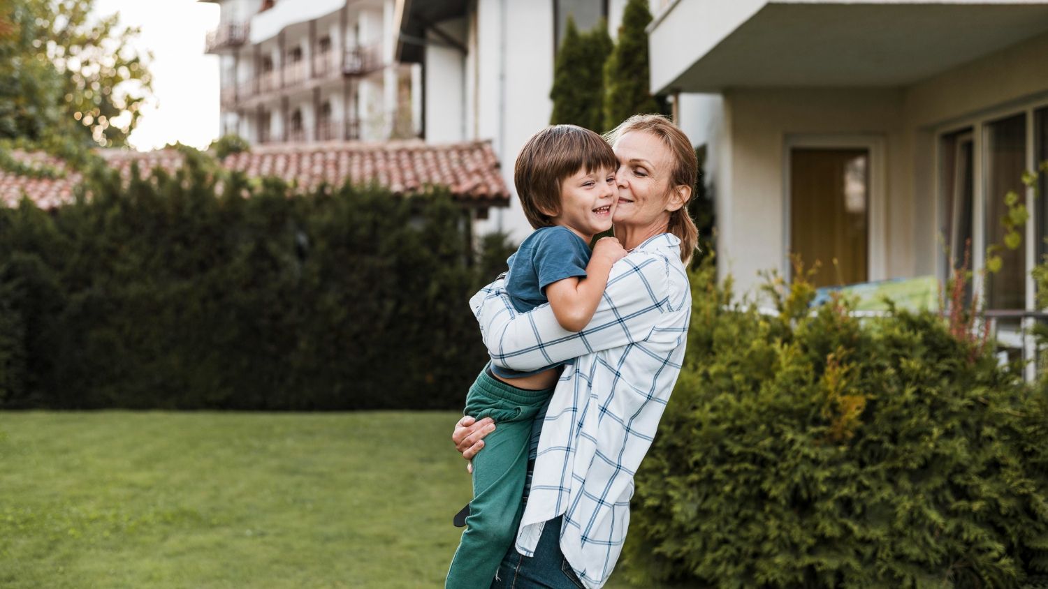 Woman hugging a smiling child in a yard outside a house