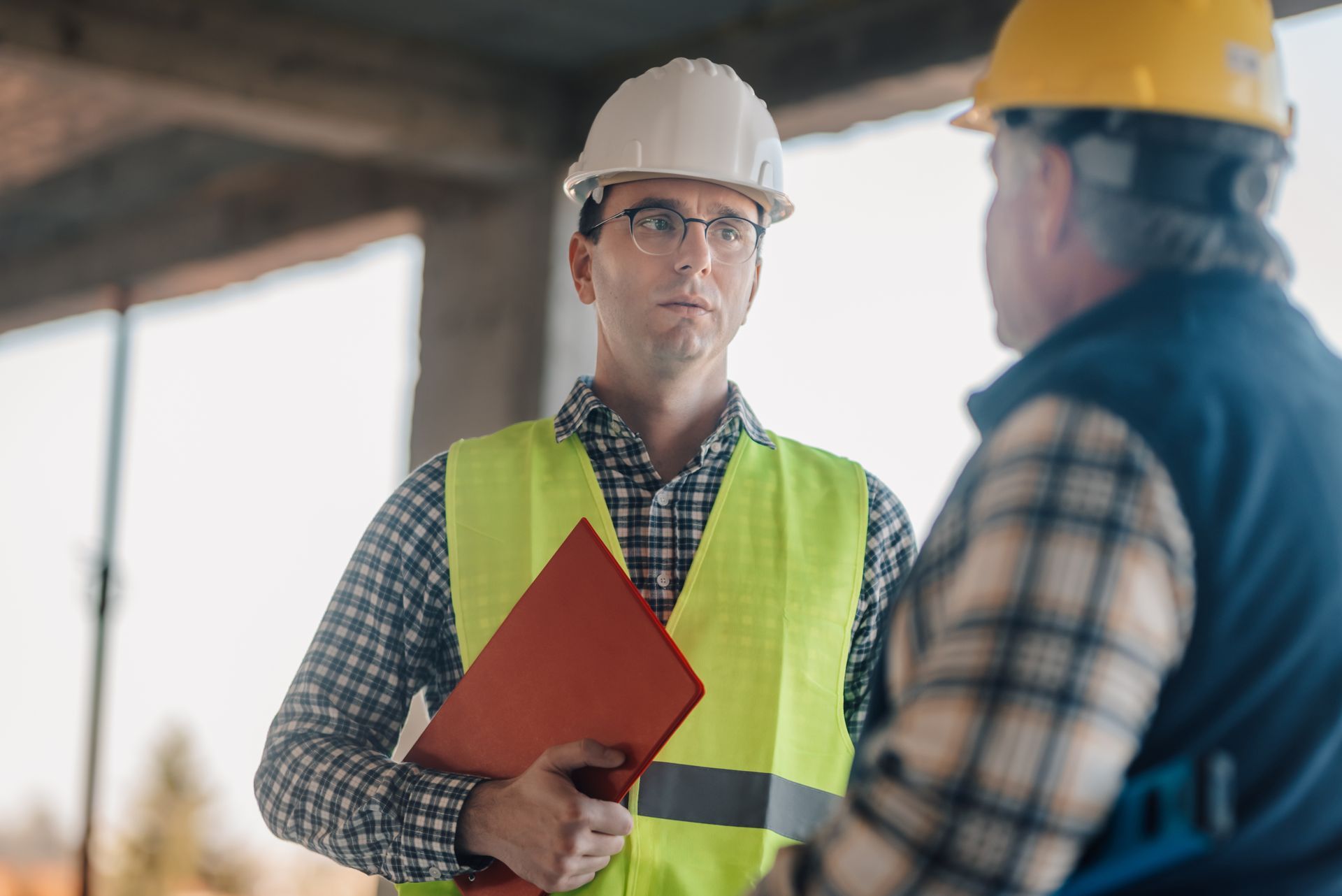Two construction workers in hard hats and safety vests talking at a building site