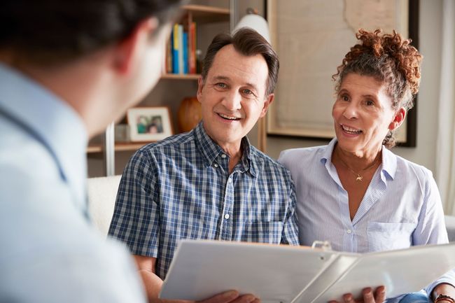 Two people smiling during a consultation, looking at a booklet with a blurred person in the foreground.