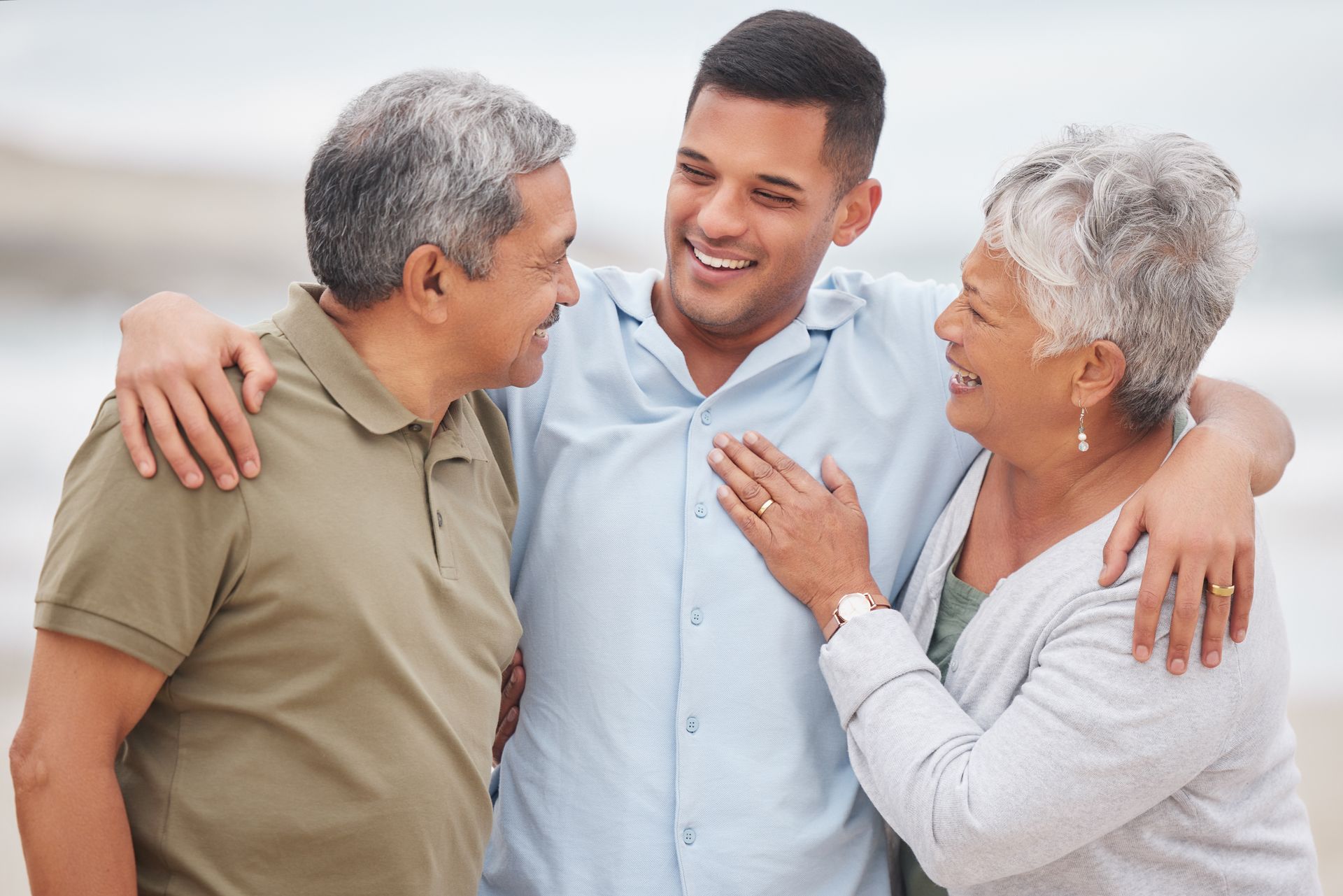 Three people smiling and embracing on a beach at sunset