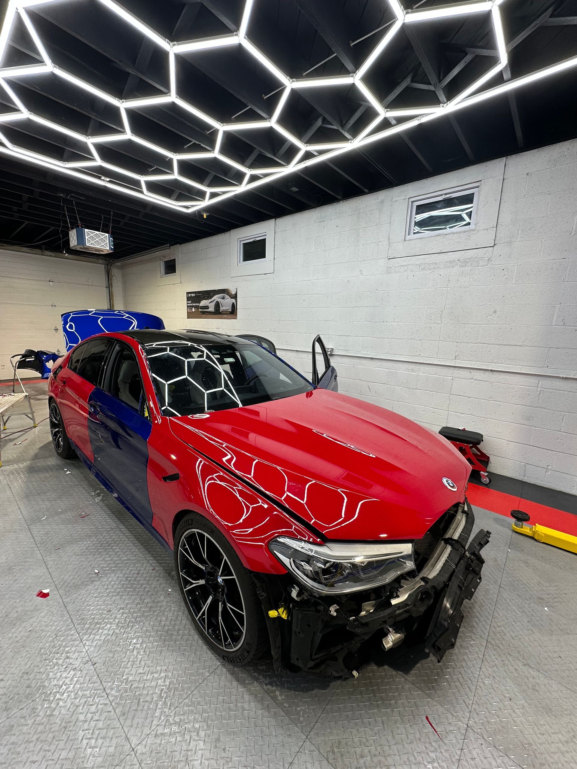 Red sports car with front-end damage in a garage under bright geometric ceiling lights