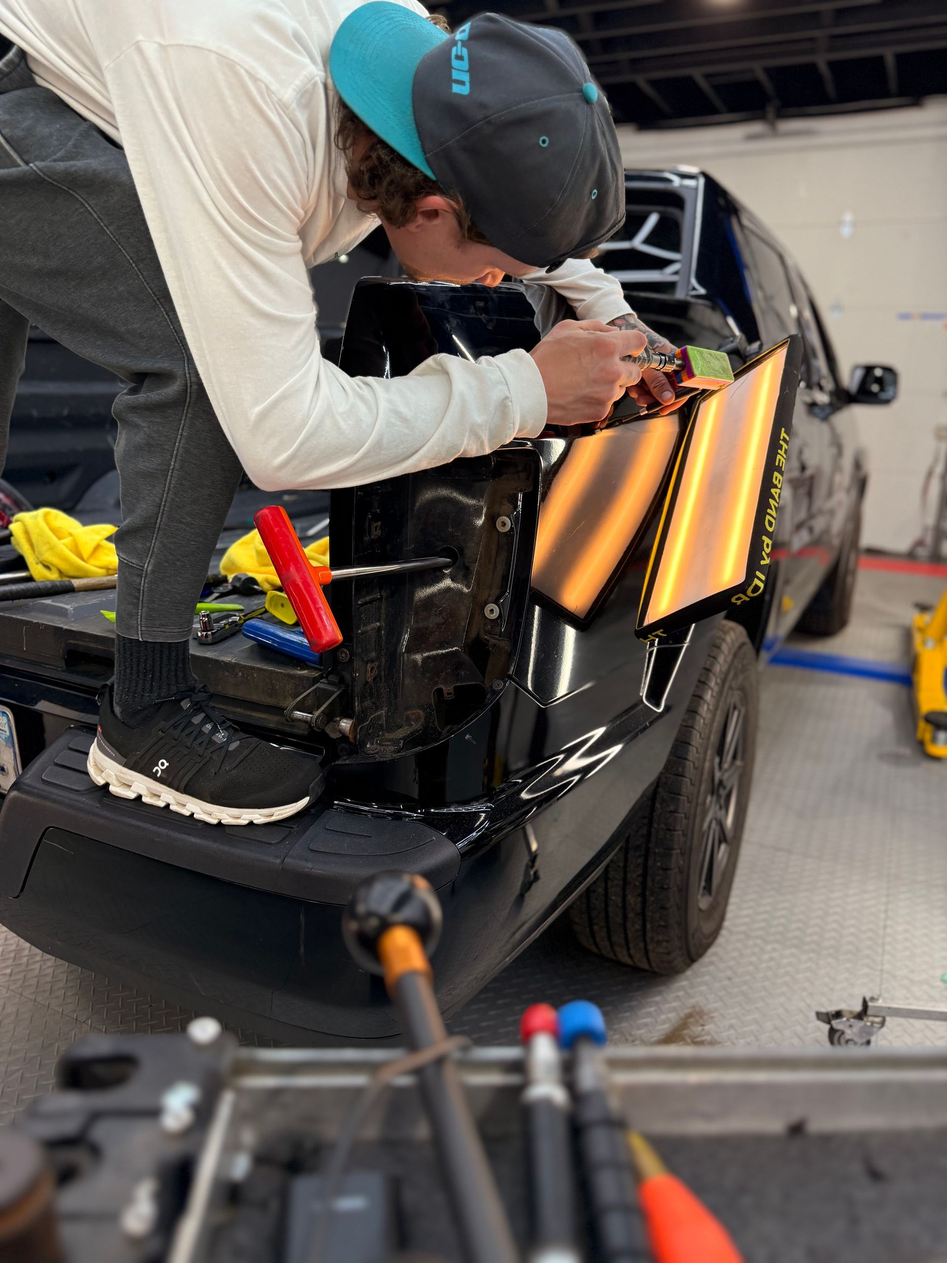 A person uses a specialized tool to repair a dent on a red car body, guided by a yellow reflective light board.