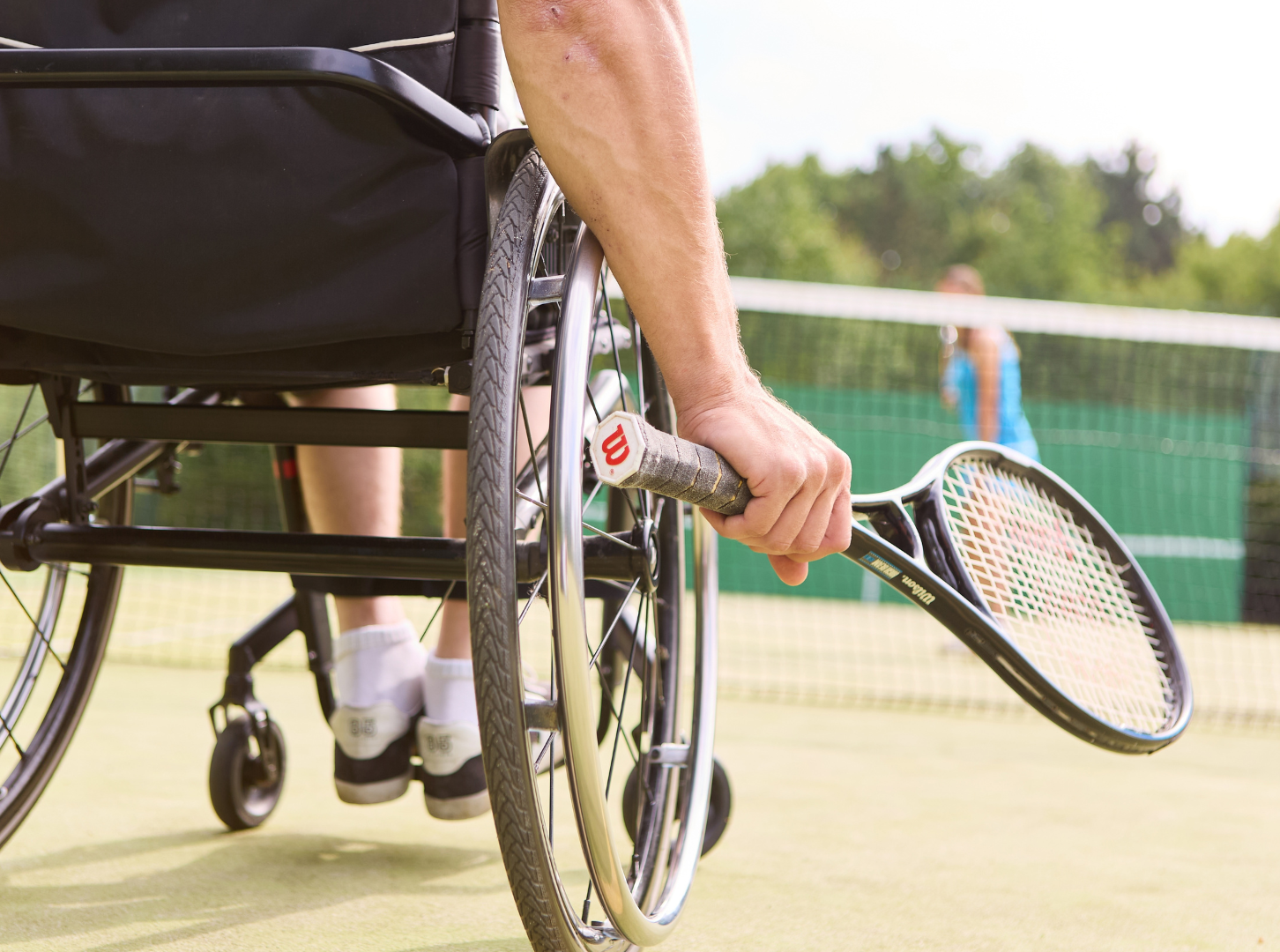 Eine Person im Rollstuhl hält einen Tennisschläger auf einem Tennisplatz.