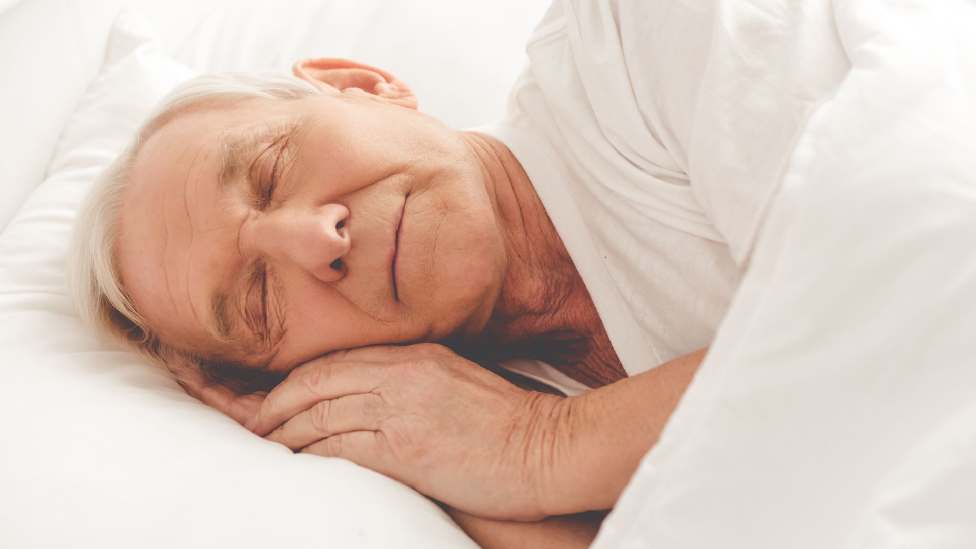 Ein älterer Mann schläft in einem Bett unter einer Decke.
