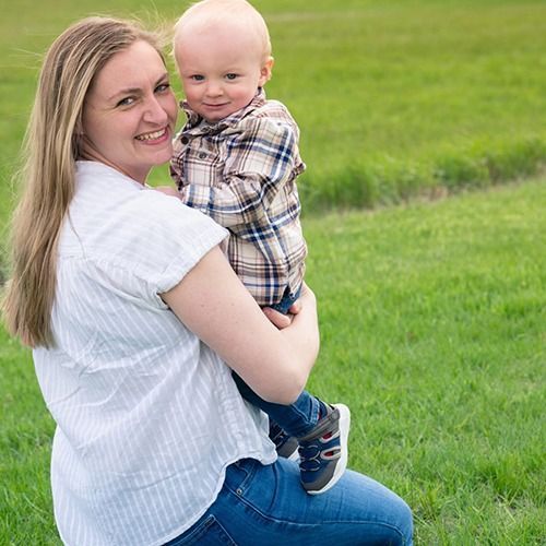 Woman holding a smiling baby outdoors in a grassy field