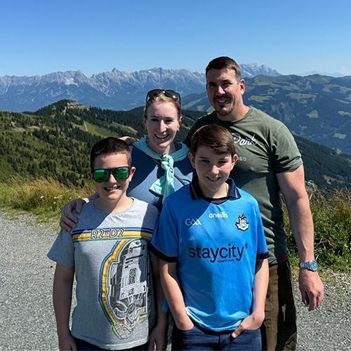 Four people posing outdoors with mountains in the background on a sunny day