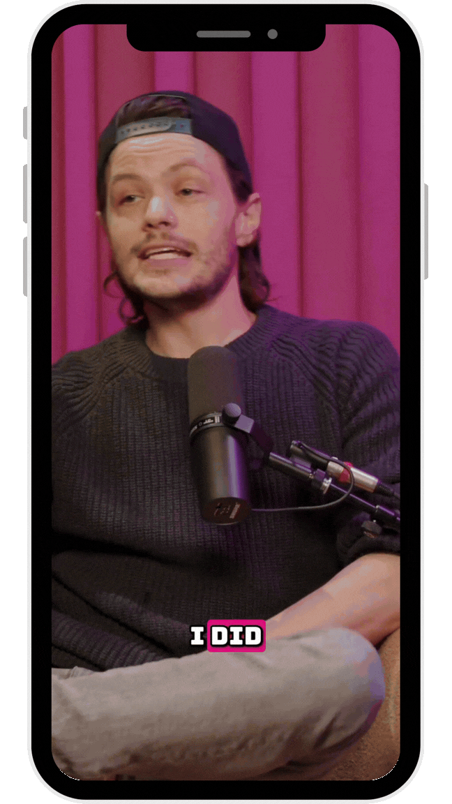 A person wearing a cap and dark sweater speaks into a microphone in front of a pink background, with the text 