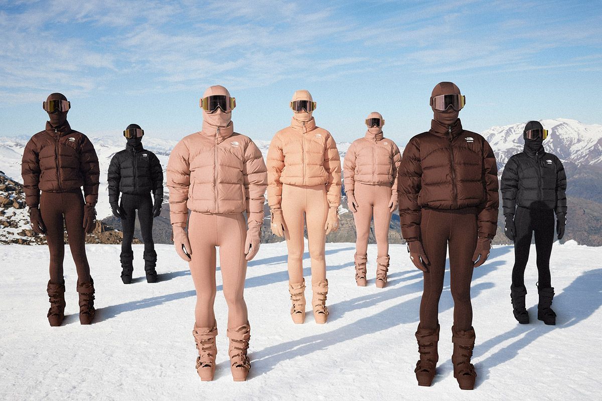 People wearing coats in natural skin tones standing on snow with mountains in the back