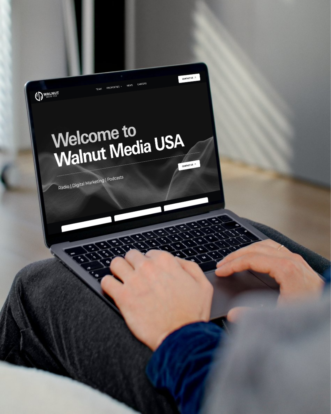 Person typing on a laptop displaying “Welcome to Walnut Media USA” in a dark workspace.