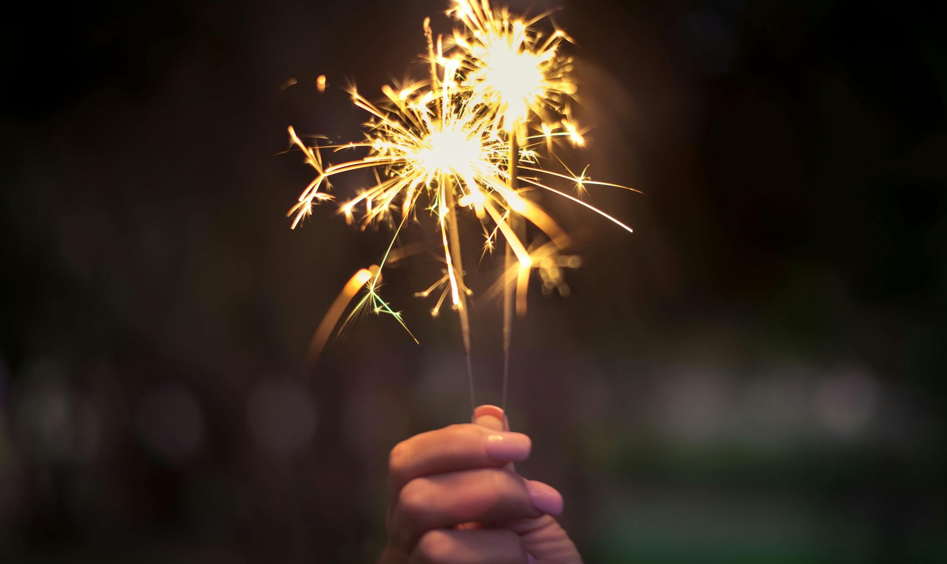 A person is holding a sparkler in their hand at night.