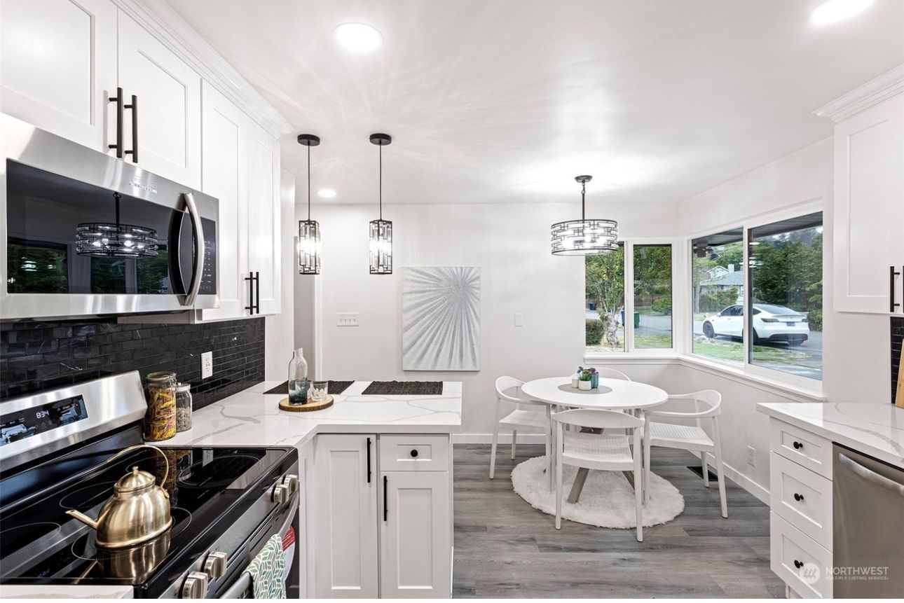 A kitchen with white cabinets , a stove , a microwave , a table and chairs