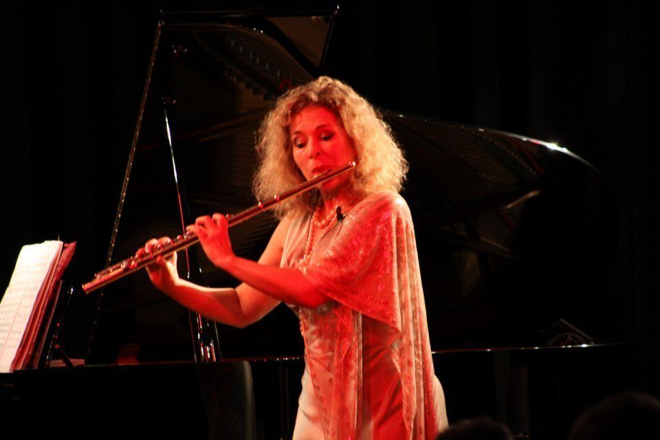 A woman is playing a flute in front of a piano