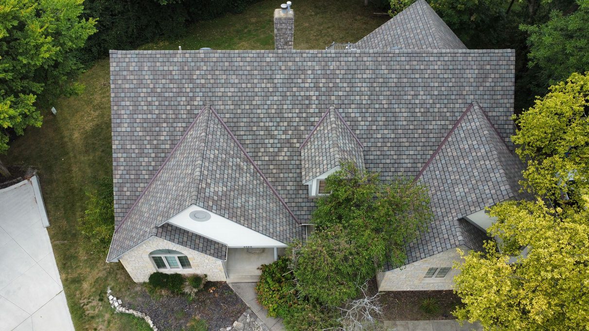Aerial view of house with gray roof, chimney, and surrounding greenery.