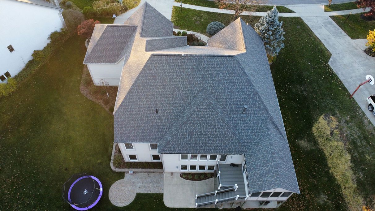 Aerial view of a gray-roofed house with a patio, trampoline, and lawn.