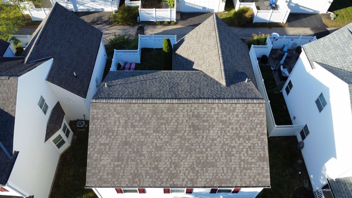 Aerial view of a gray-shingled roof on a white house, surrounded by other houses and yards.