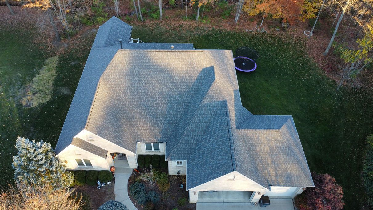 Overhead view of a house with a gray roof and a trampoline in the yard, surrounded by trees with fall foliage.