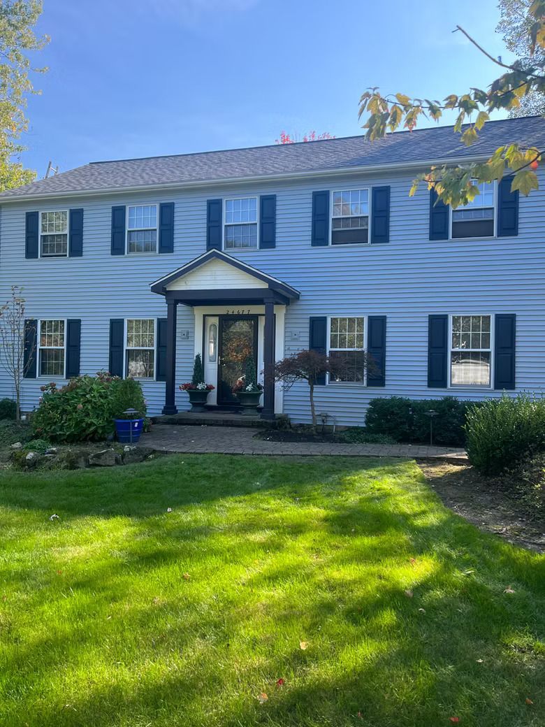 Two-story light blue house with dark blue shutters, centered door, and green lawn.