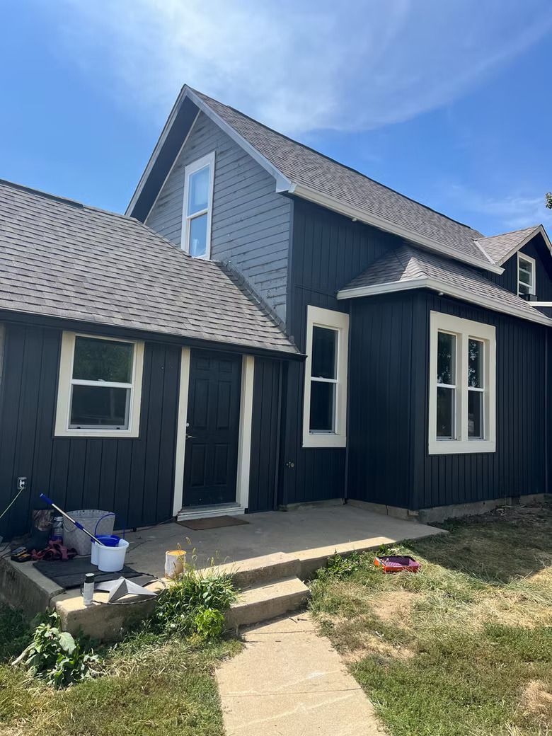 Dark blue house with white trim, gray roof, and a concrete path. Sunny day.