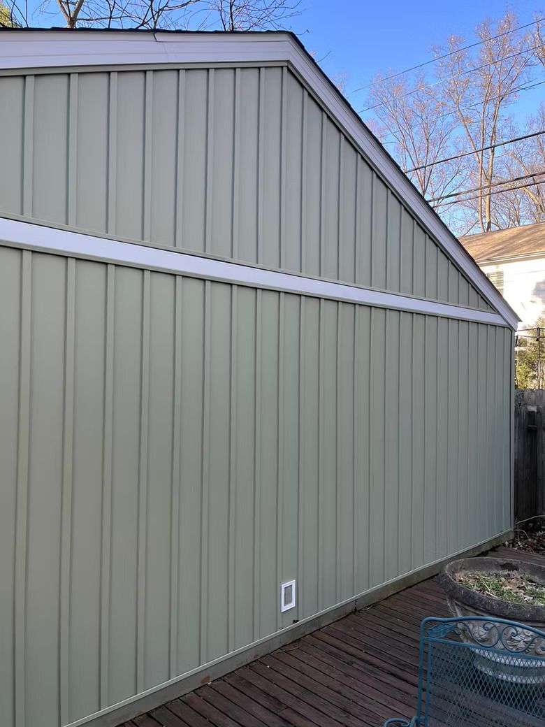 Green-sided building with vertical lines and white trim, on a wooden deck under a blue sky.