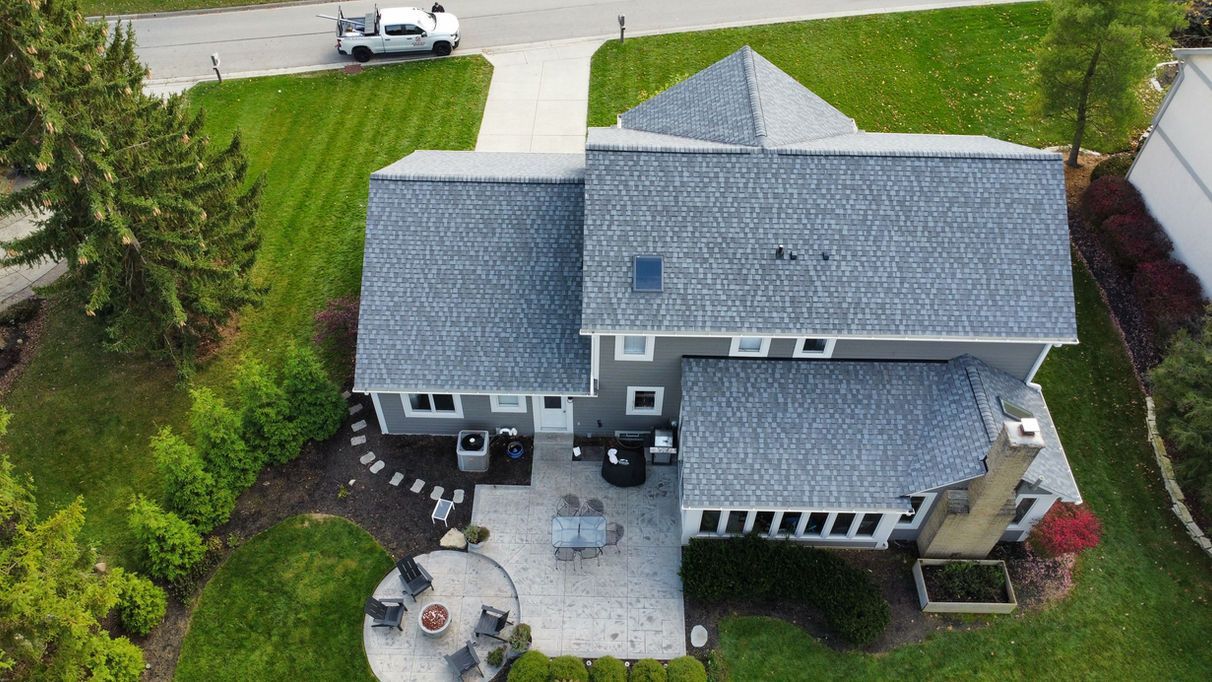 Aerial view of a gray house with a patio, lawn, and driveway. A white car is parked.