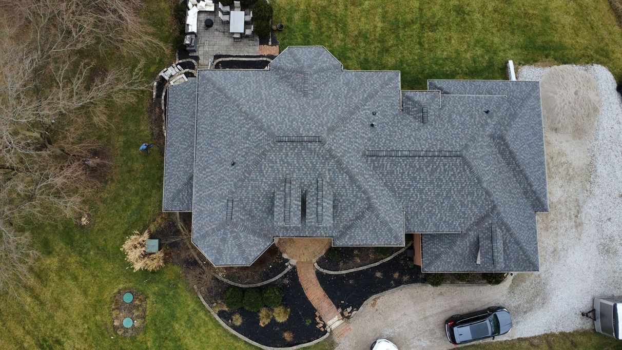 Overhead view of a house with a gray shingle roof, gravel driveway, and surrounding green lawn.